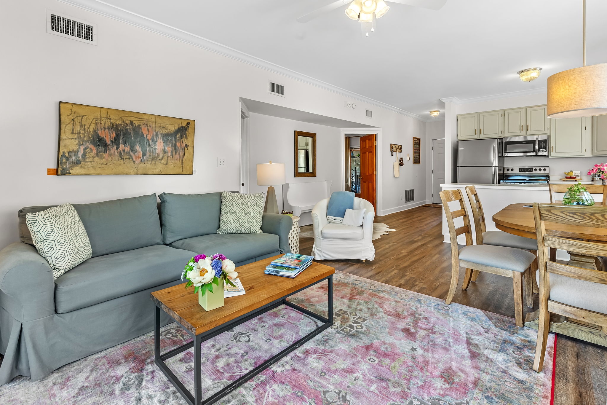 Main Living Area with comfortable blue-green couch, wood-topped coffee table, cozy armchair, dining table & chairs, and kitchen in background