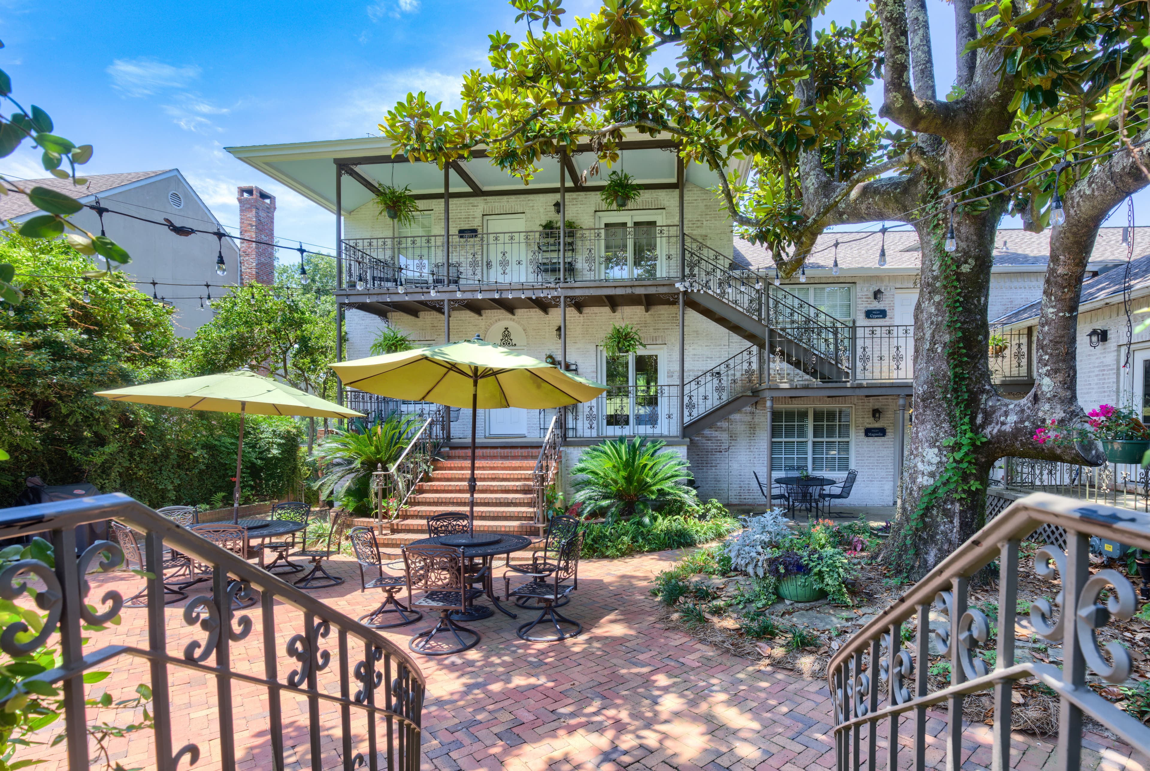 Courtyard entrance to suite with decorative metal railing, patio tables with chairs and large yellow umbrellas