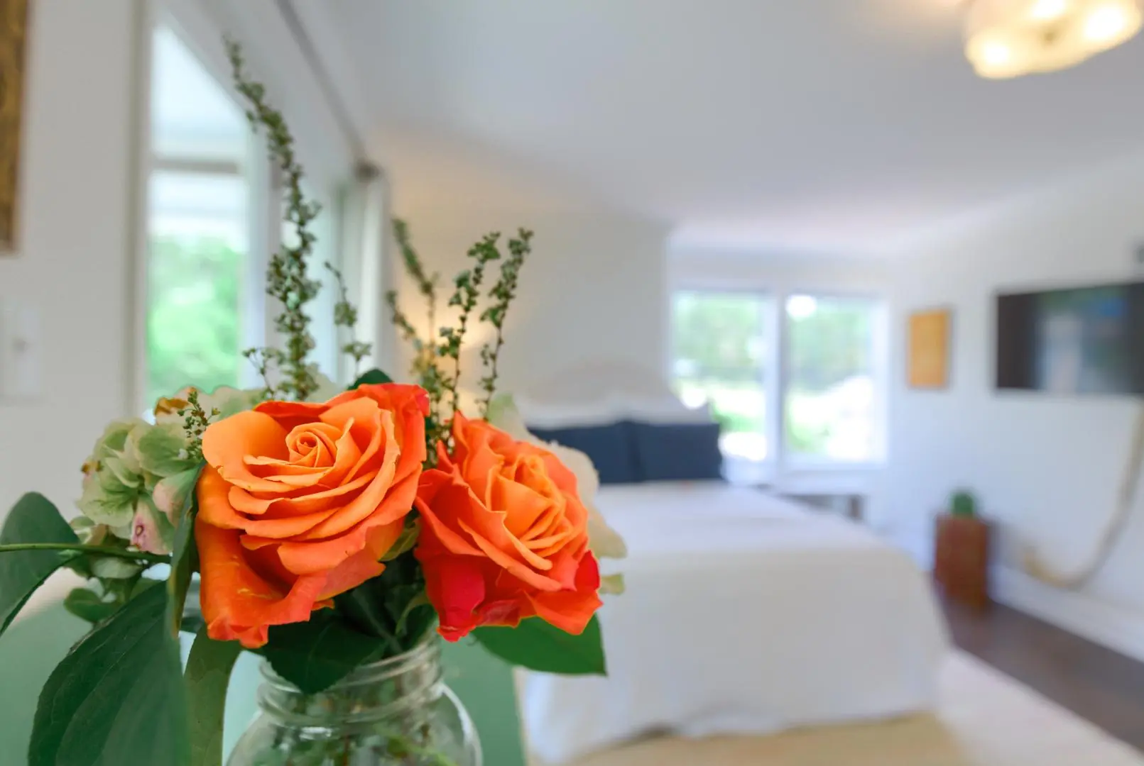 A close-up of orange roses in a jar, with a softly lit bedroom in the background.