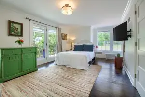Bright and inviting bedroom with a green dresser, a white bed, and large windows letting in natural light.