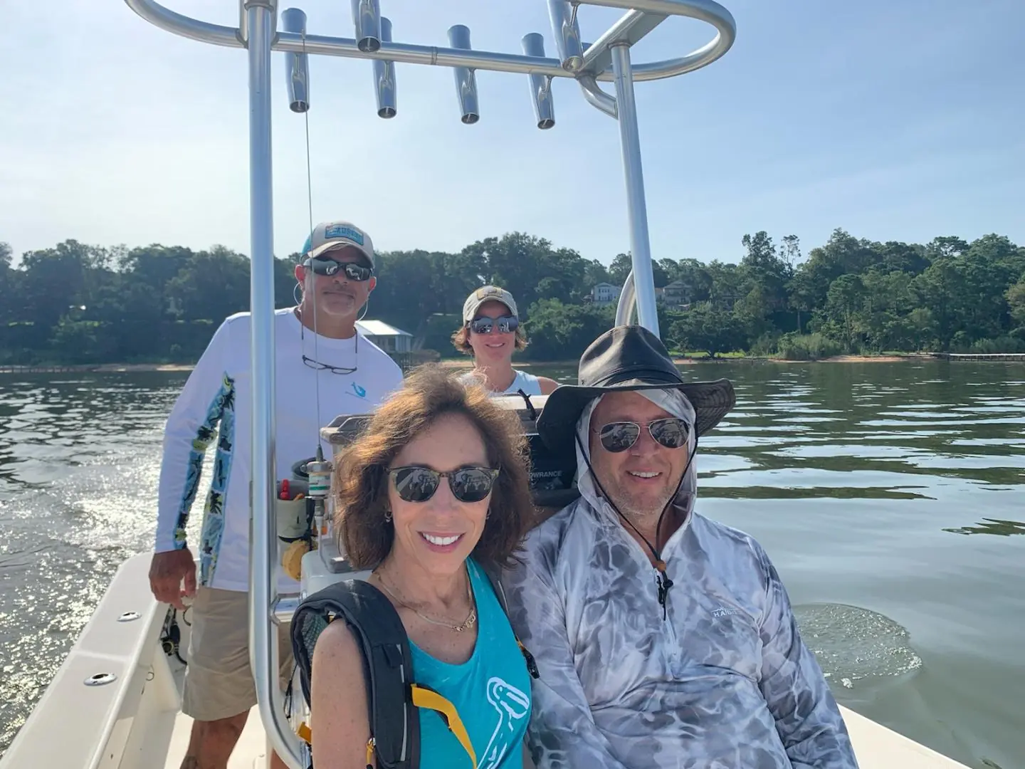 Group of four people smiling on a boat in calm waters surrounded by trees.