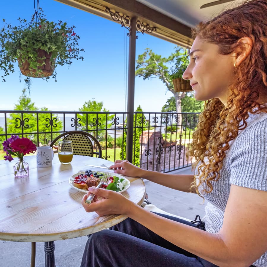 A woman eating breakfast at an outside table looking out at the bay