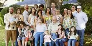 A large family poses together outdoors, gathered around a tree.