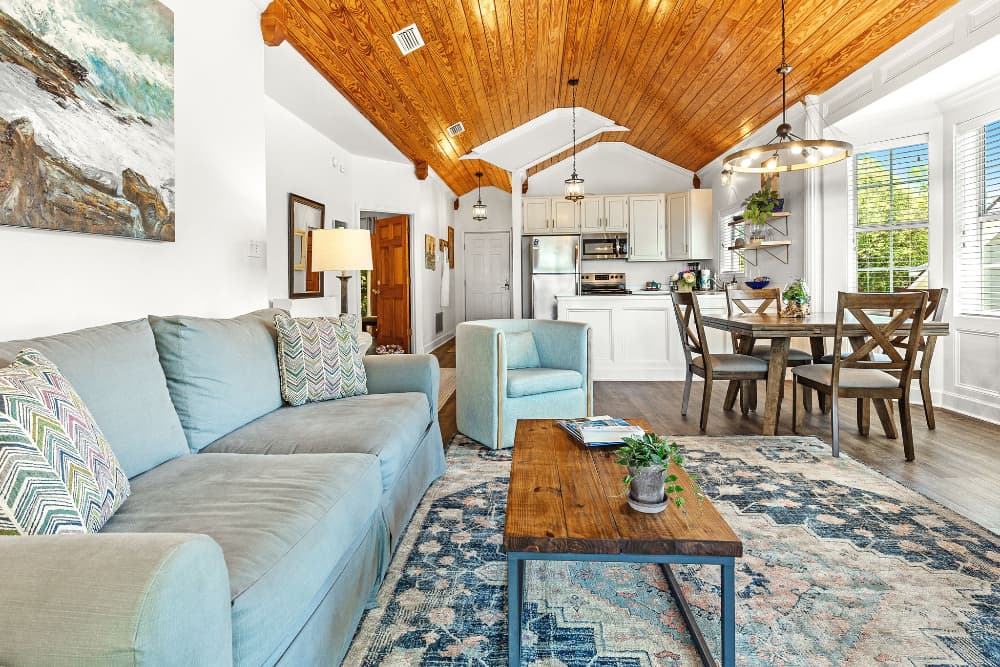 A cozy living area with a blue sofa, wooden dining table, and a vaulted ceiling featuring warm wood accents.